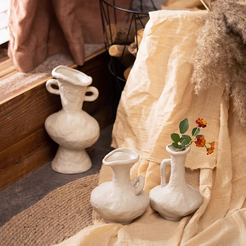 Three rustic white ceramic flower vessels styled beside natural textiles