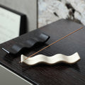Wave ceramic incense trays in milk white and black on dark wood furniture