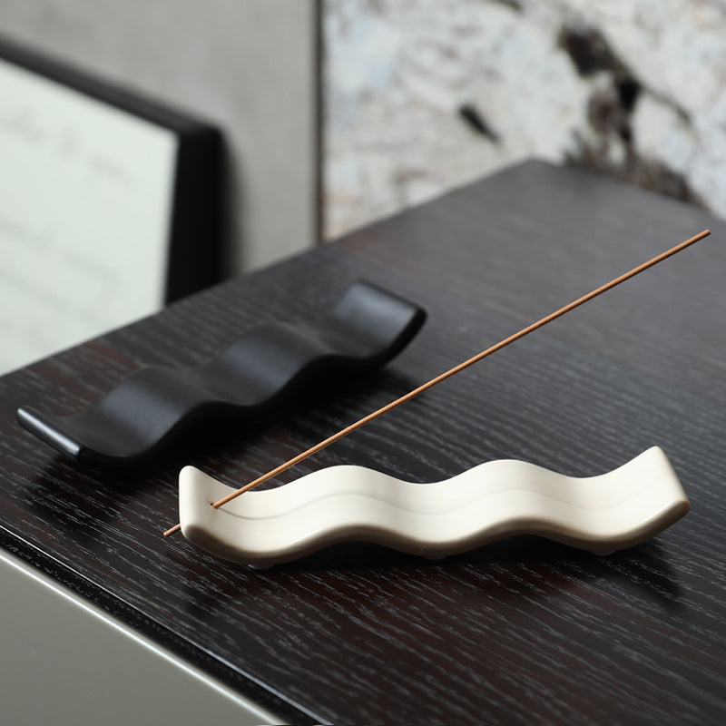 Wave ceramic incense trays in milk white and black on dark wood furniture
