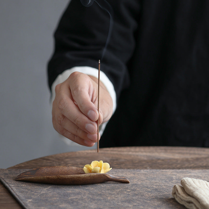 Hand placing a thin incense stick into osmanthus flower ceramic incense holder
