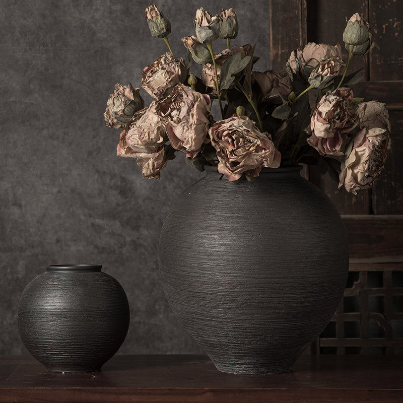 Black ribbed round ceramic vase styled with dried flowers in a dark wood interior