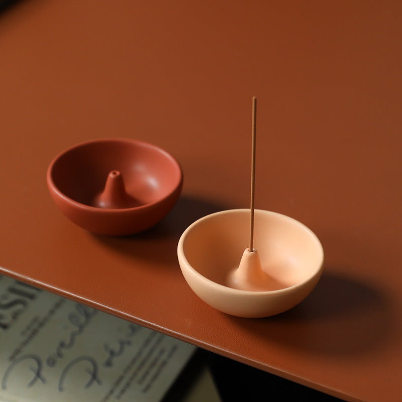 Round ceramic incense bowls in red and light coffee against warm terracotta background