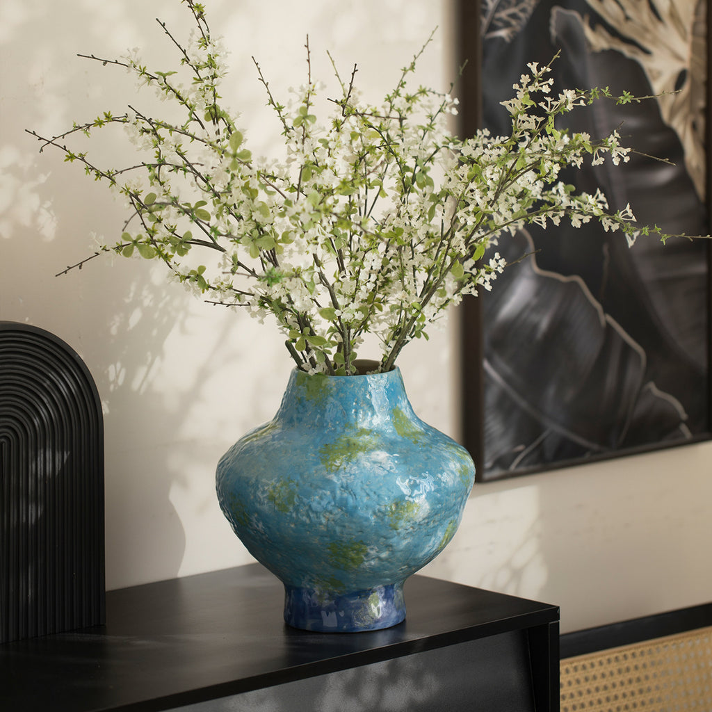 Turquoise blue mottled ceramic vase with airy white branches in modern interior
