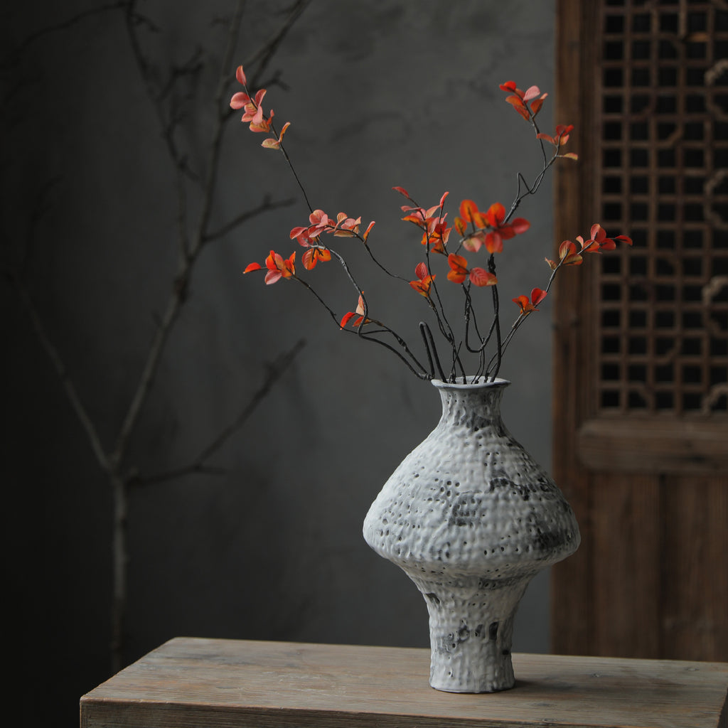 Mottled white hammered vase with orange-red blossom branches