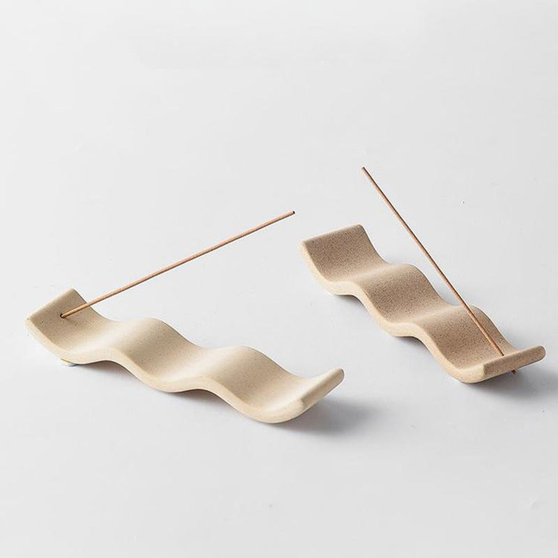 Two wavy ceramic incense trays with thin incense sticks on a light background