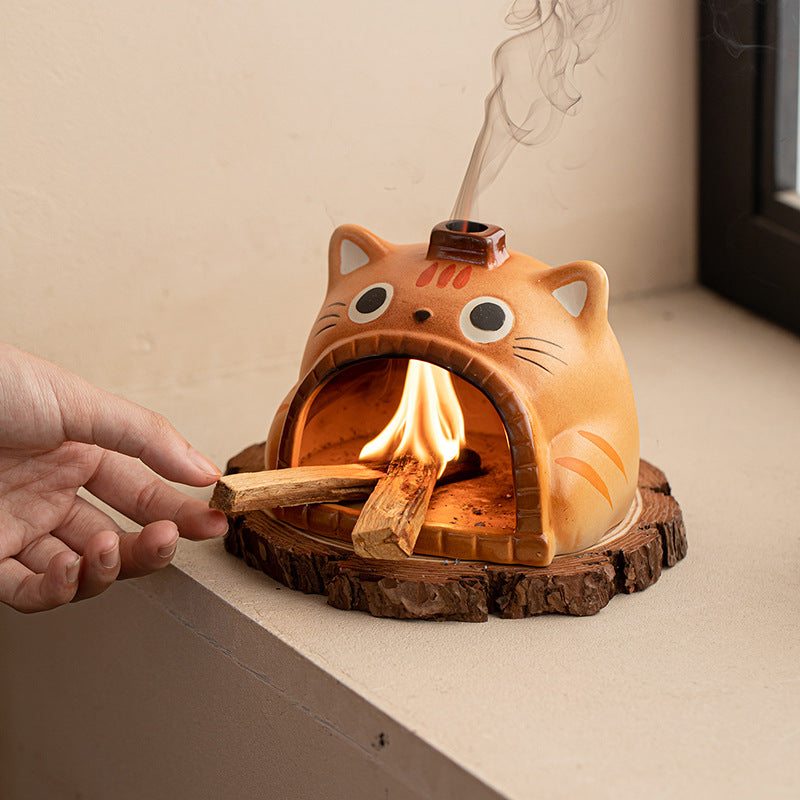 Orange cat ceramic Palo Santo burner glowing on a wooden coaster