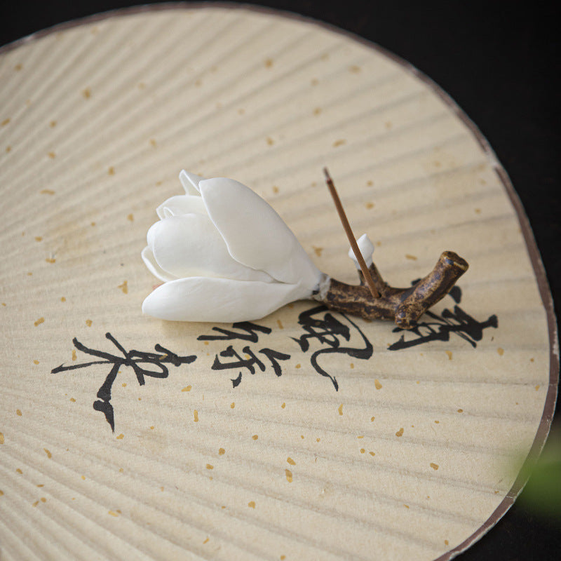 Magnolia flower incense holder with incense stick on an Asian calligraphy tray