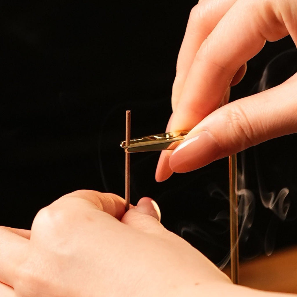 Hands securing an incense stick to the hanging incense burner clip