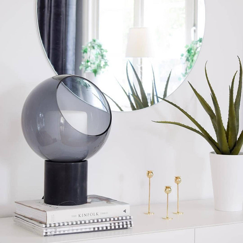 Smoked glass and marble orb lamp styled on books in bright interior