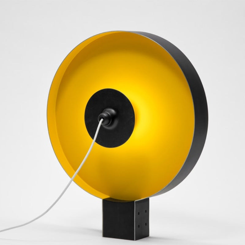 Round flying saucer table lamp showing warm gold reflector side and black square base