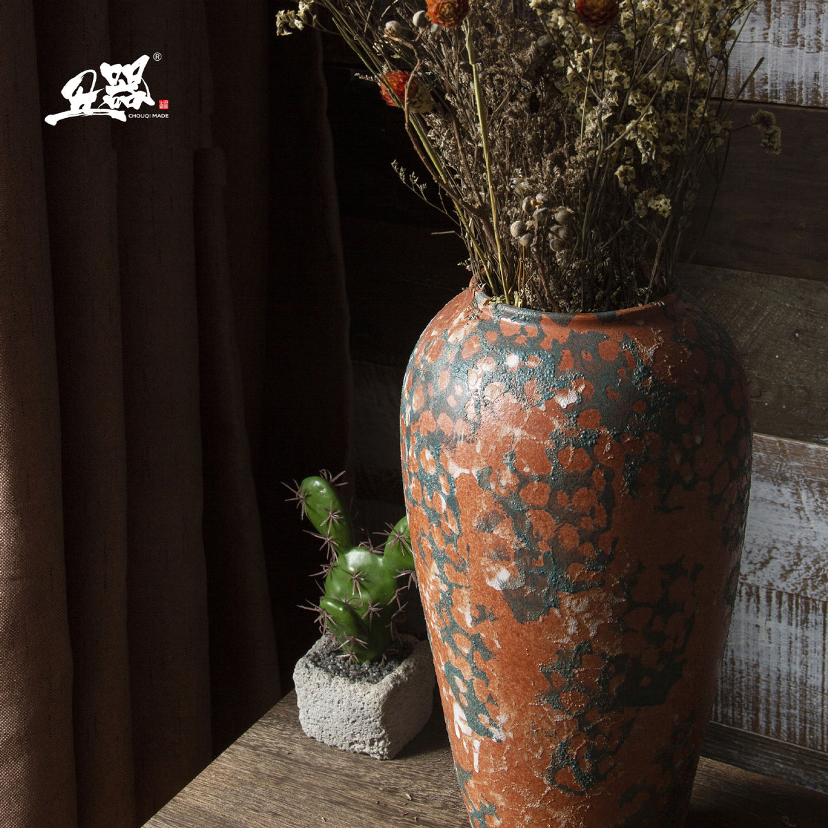 Tall terracotta orange and blue-green patina ceramic vase with dried branches