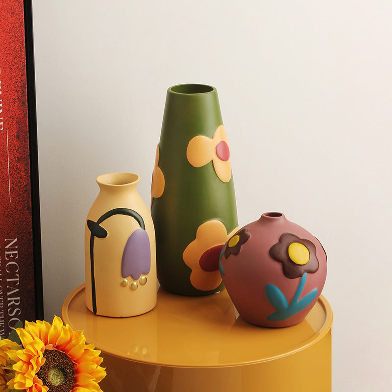 Colorful hand-painted ceramic vase trio displayed on mustard yellow table