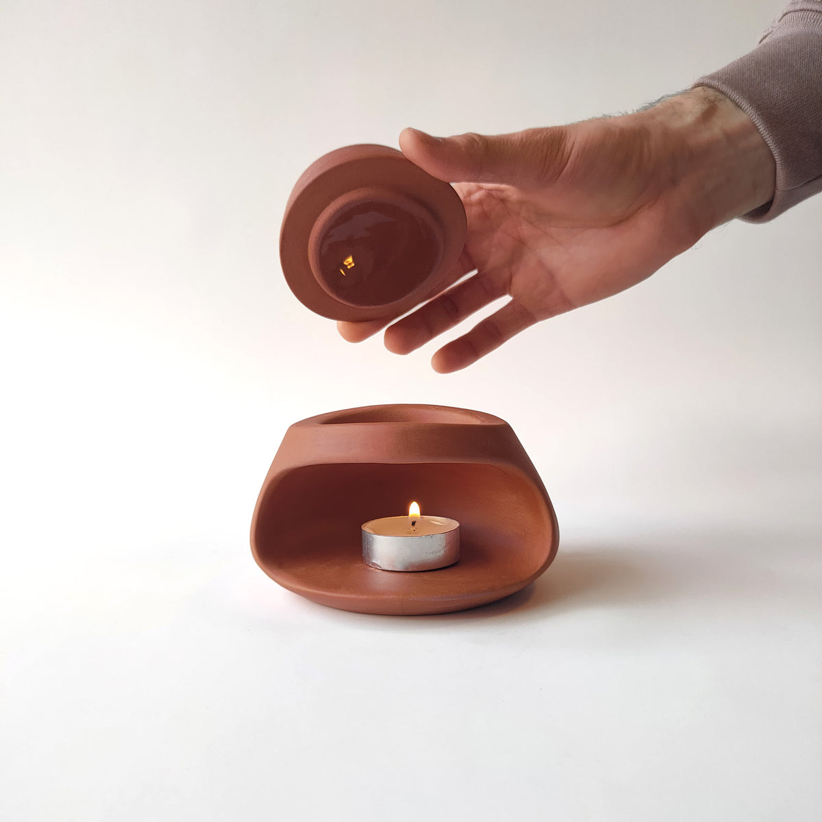 Hand lifting removable ceramic bowl from terracotta tealight aroma burner