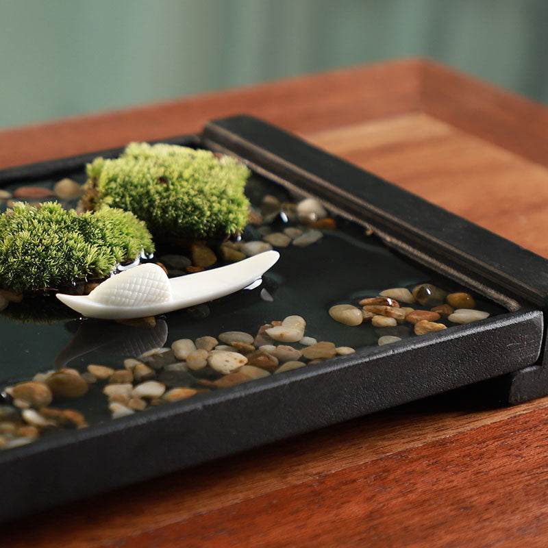 Black stone tabletop water garden with moss pebbles white ceramic boat and incense detail