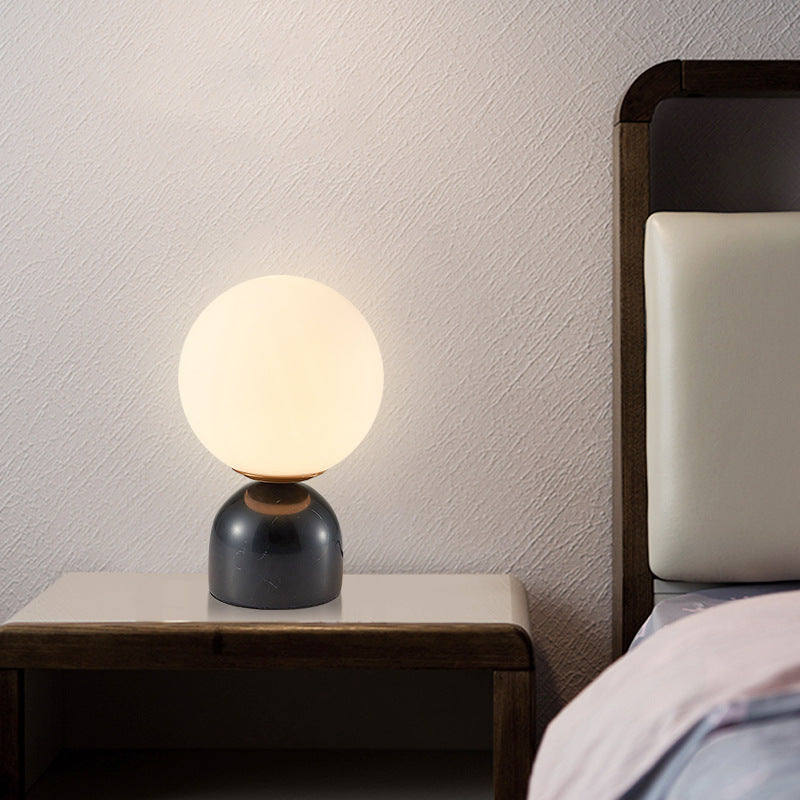 Black marble globe table lamp with frosted glass shade on bedside table
