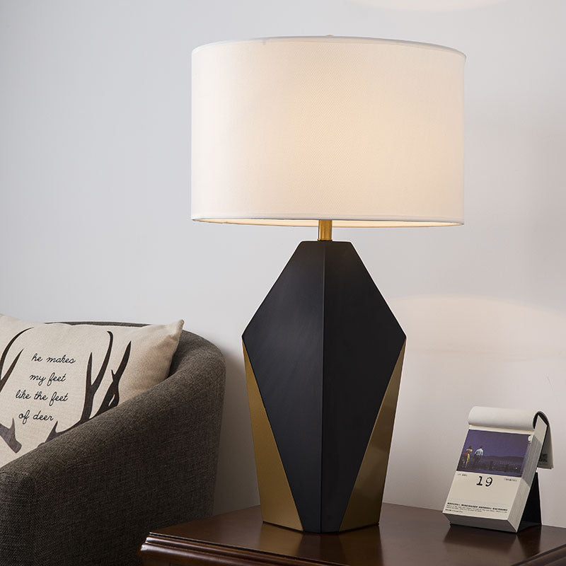 Geometric black gold bedside lamp with glowing ivory drum shade