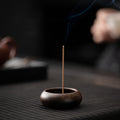Dark wood mini incense holder burning a thin incense stick on tea table