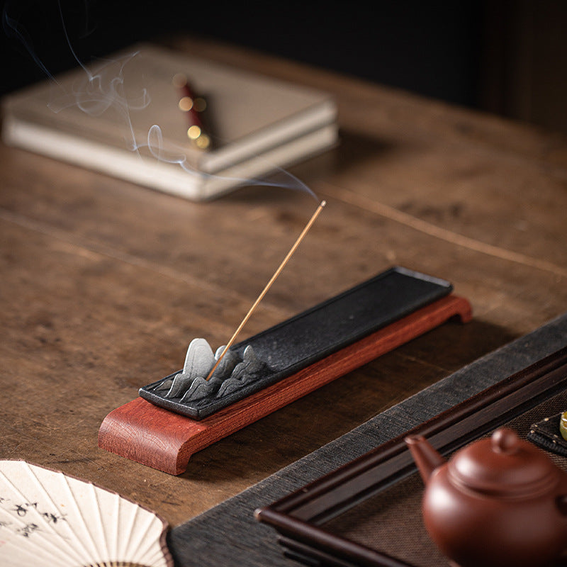 Black ceramic mountain landscape incense tray with wood base styled beside tea ware