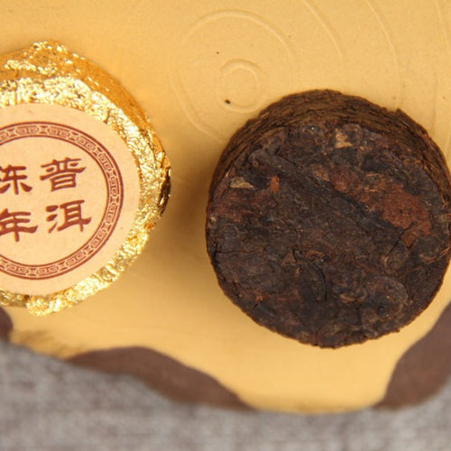2003 aged Menghai ripe Pu-erh mini cake beside its gold foil wrapper