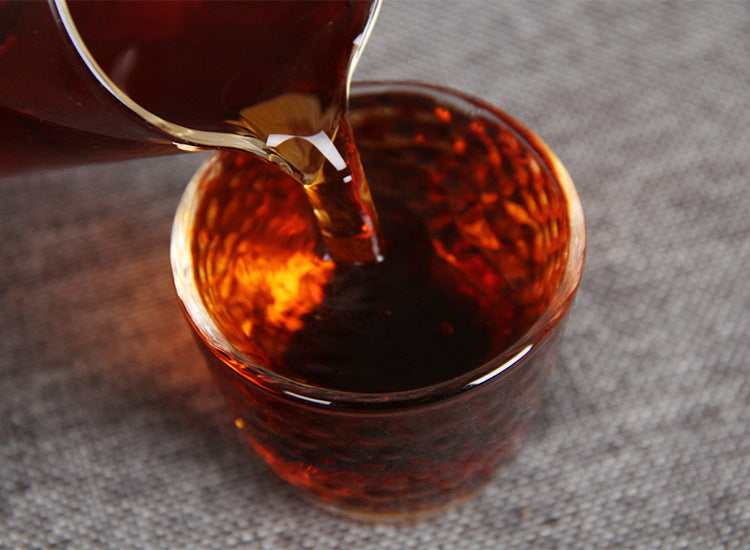 Deep red-brown liquor from aged ripe Pu-erh tea being poured