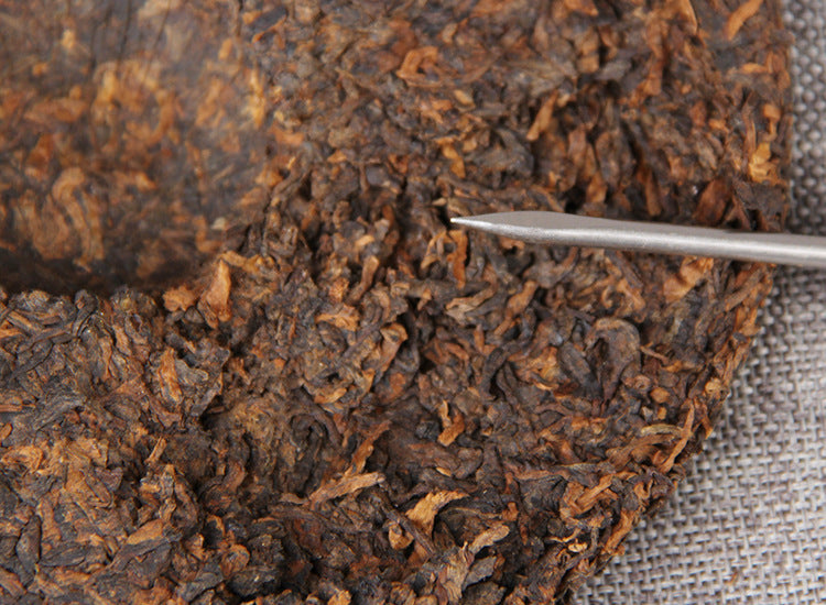 Aged ripe Pu-erh cake being portioned with a wooden tea pick