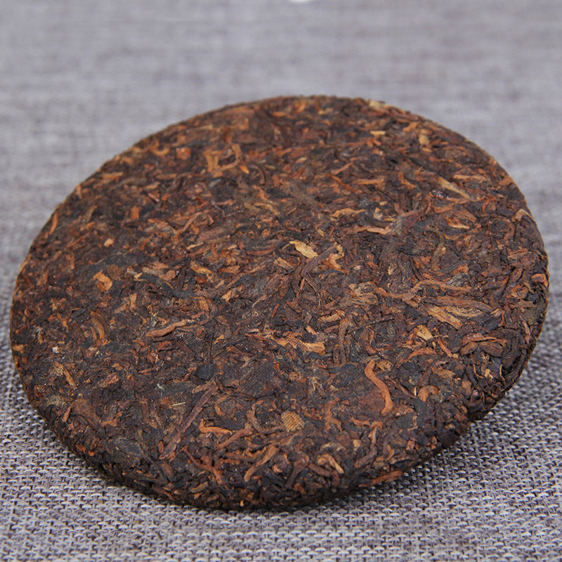 Unwrapped 2009 Golden Bud ripe Pu-erh tea cake showing compressed leaves
