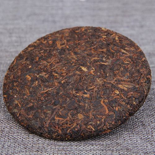 Unwrapped 2009 Golden Bud ripe Pu-erh tea cake showing compressed leaves
