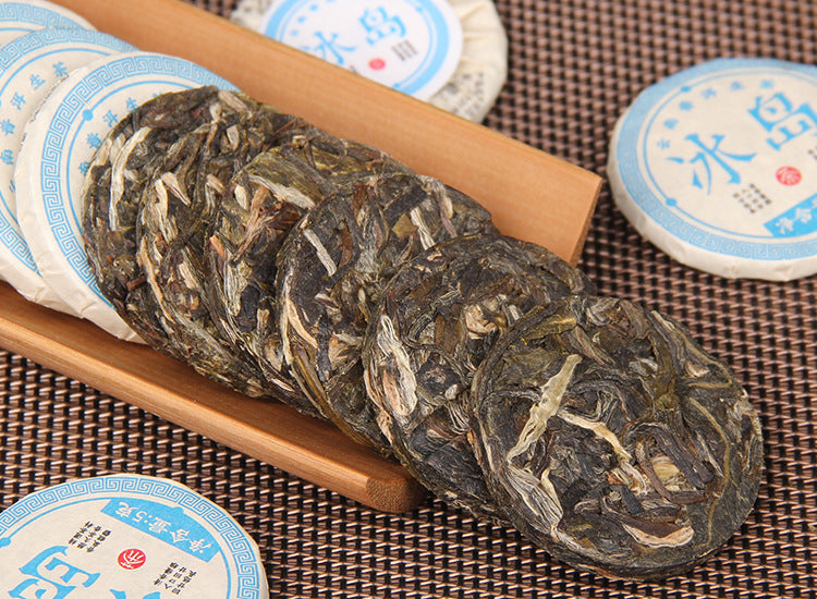 Brewed 2023 Blue Xiaobingdao raw Pu-erh showing golden liquor and mini tea cake packaging