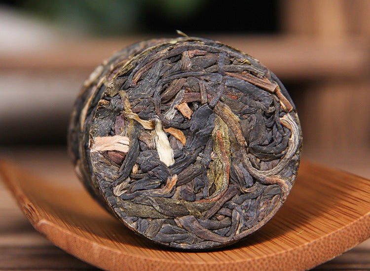 Close-up unwrapped 2023 Xigui raw Pu-erh mini cake with visible leaf material