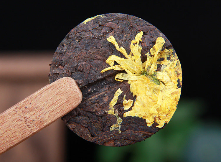 Close-up of chrysanthemum ripe Pu-erh mini cake showing whole yellow flower pressed into ripe tea