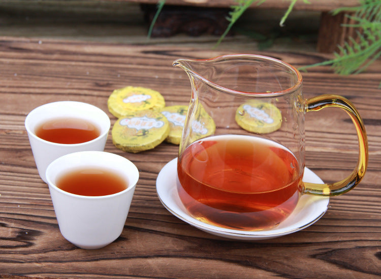 Amber-red brewed chrysanthemum ripe Pu-erh served with wrapped mini tea cakes