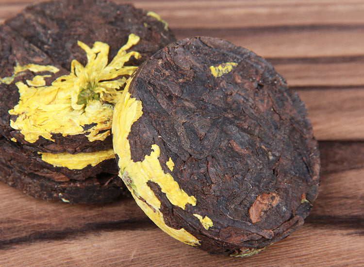 Two unwrapped chrysanthemum ripe Pu-erh mini cakes with visible yellow chrysanthemum petals