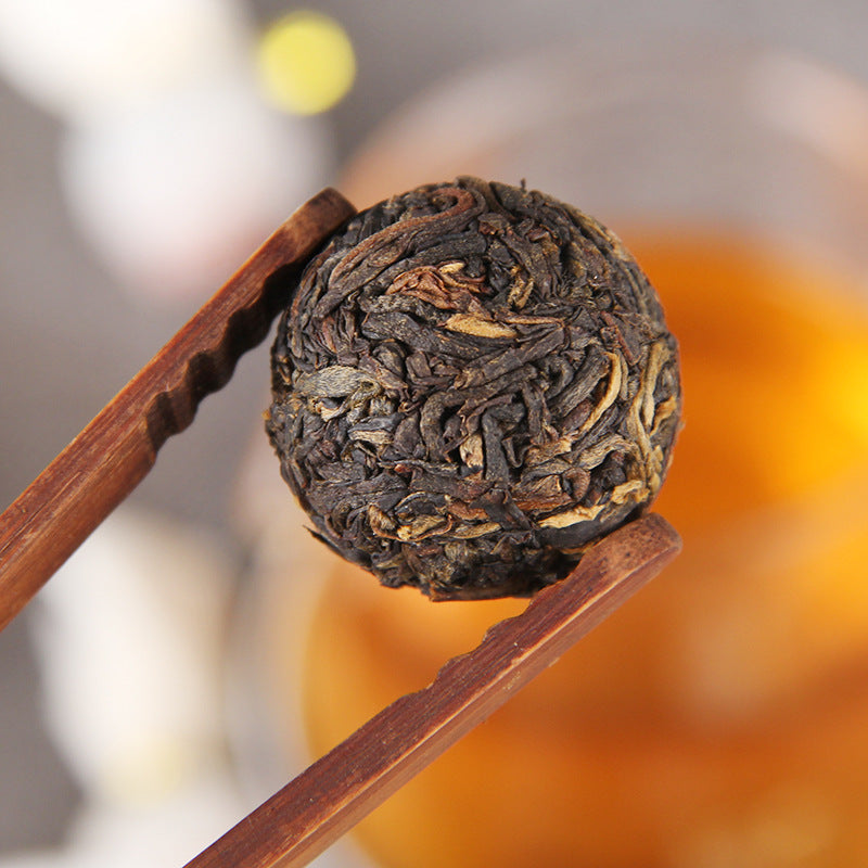 Single compressed Dianhong black tea dragon pearl held with tea tongs