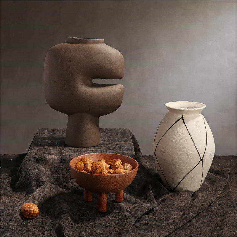 Brown sculptural cutout ceramic vase styled with white vessel and tripod bowl