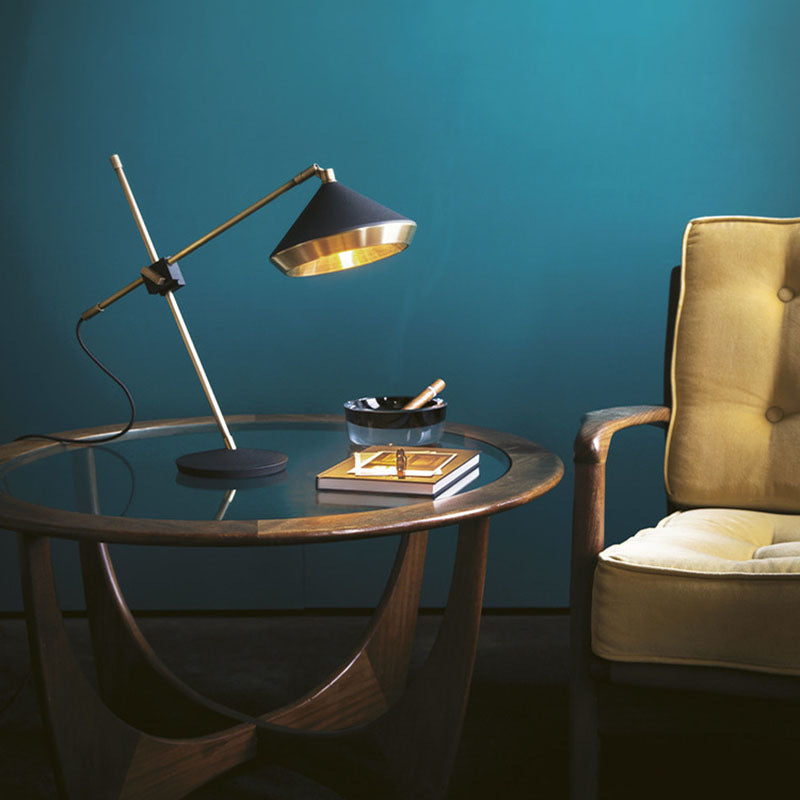 Black and antique-brass sculptural task lamp beside a lounge chair