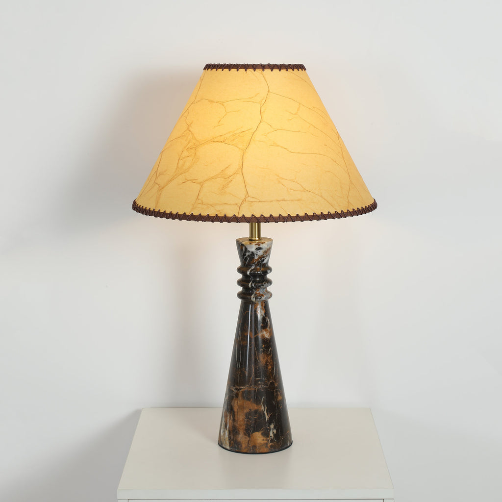 Black-gold marble column table lamp with parchment shade on a white pedestal