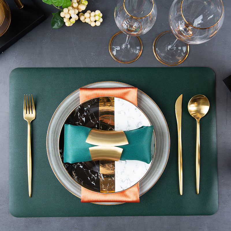 Contemporary luxury table setting combining grey dinnerware, marble accent plate, gold flatware and green placemat