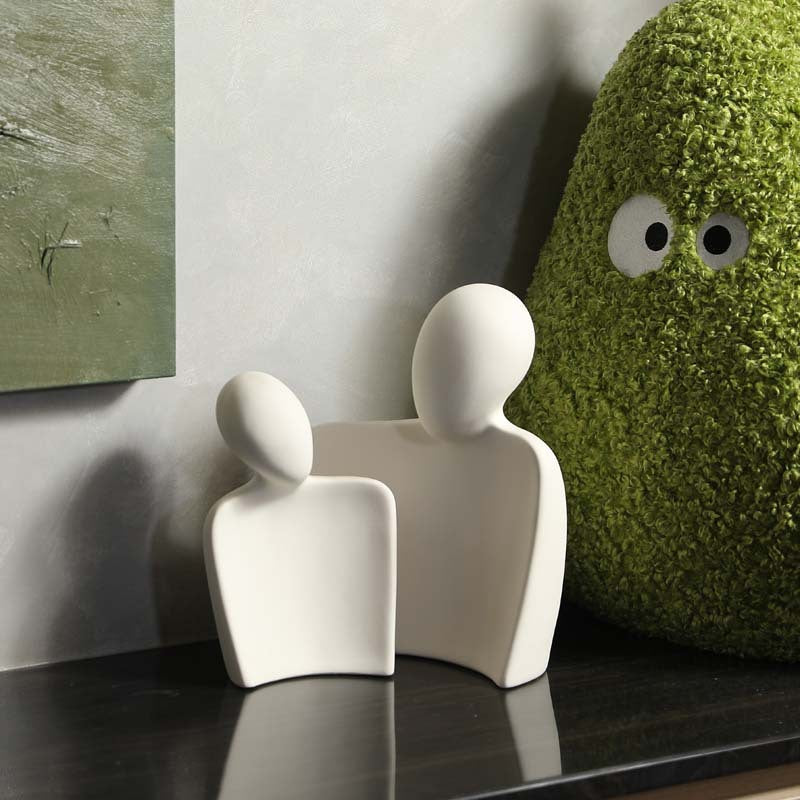 White ceramic couple sculpture beside green sculptural decor