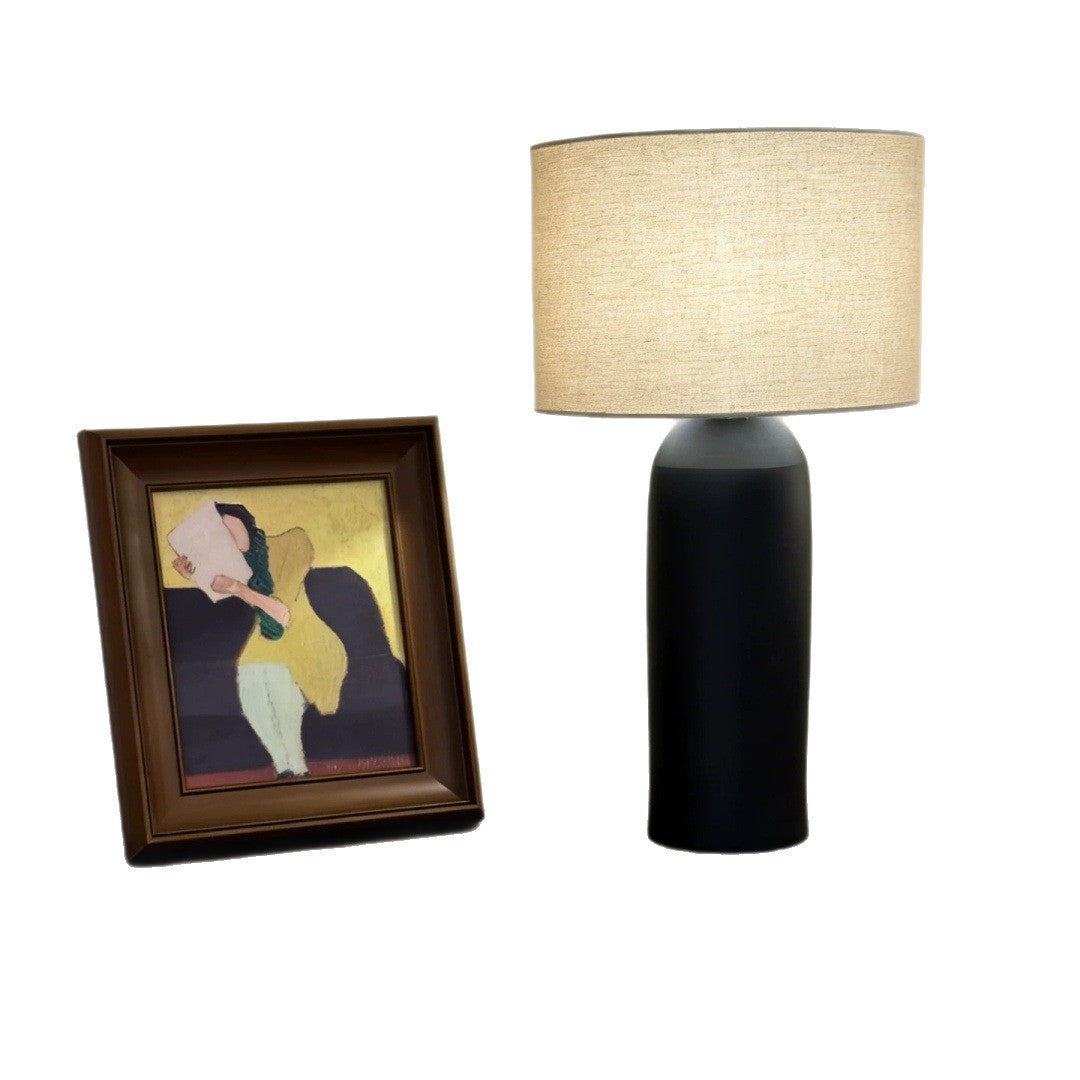 Black cylindrical ceramic table lamp beside framed artwork