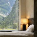 Tall black cylindrical ceramic table lamp with linen drum shade in bedroom