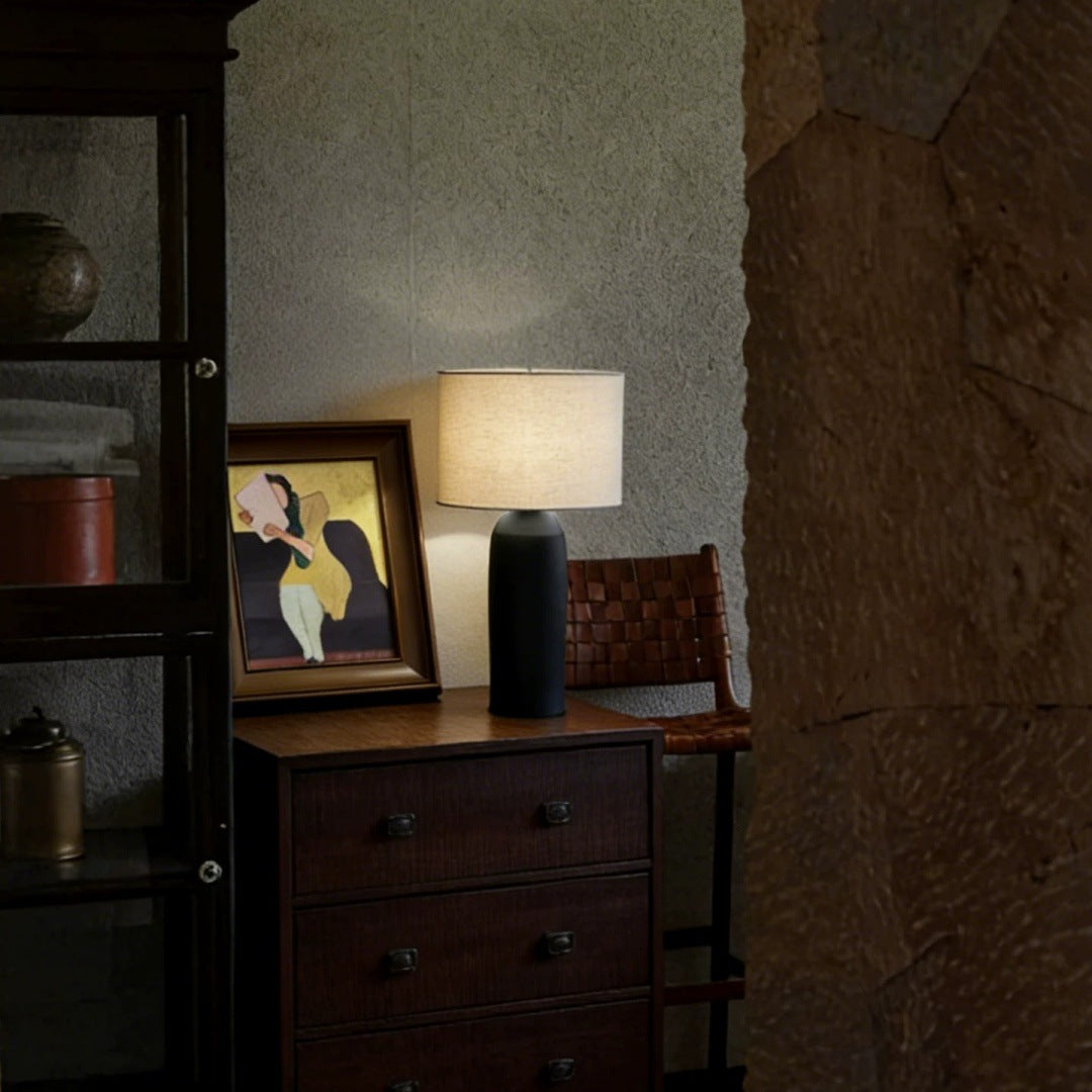 Black ceramic cylinder lamp on dark wood cabinet in wabi-sabi interior