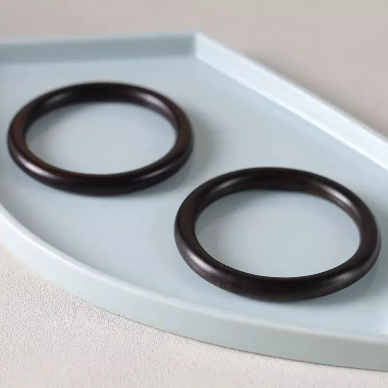 Dark blackwood-style round wooden bangle bracelets displayed on a pale ceramic tray