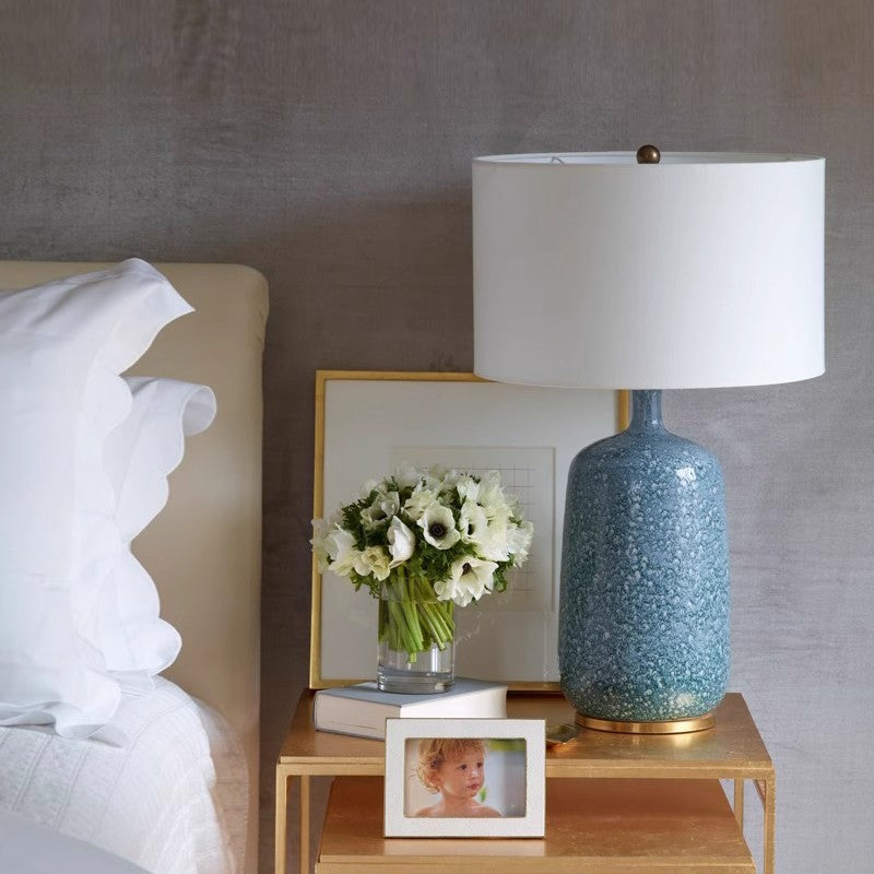 Tall blue ceramic table lamp with white shade on bedside table