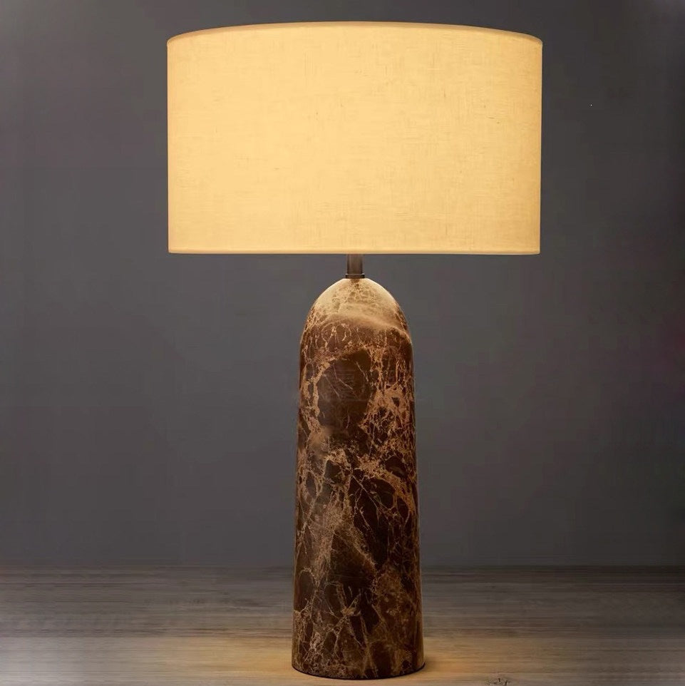 Brown veined natural marble column table lamp glowing with linen drum shade