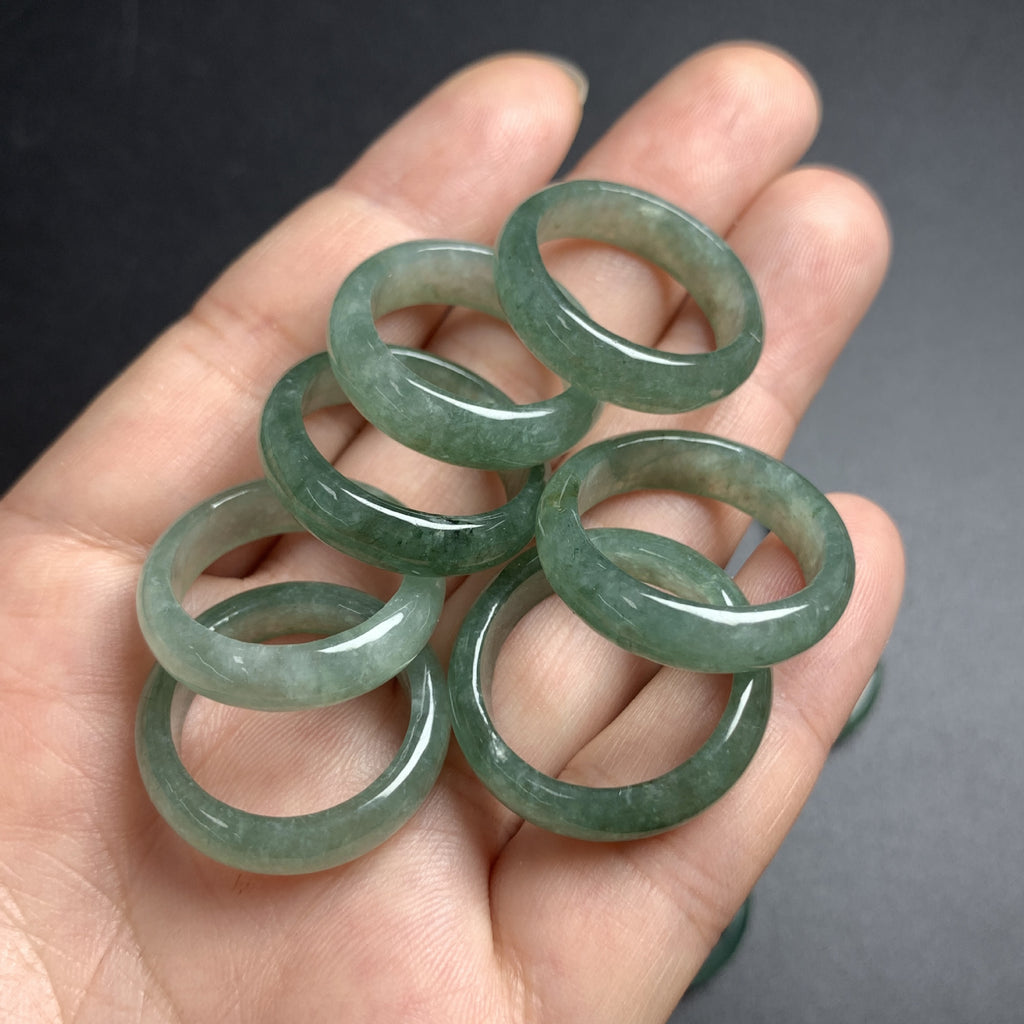 Selection of green jadeite rings held in hand showing natural color variation