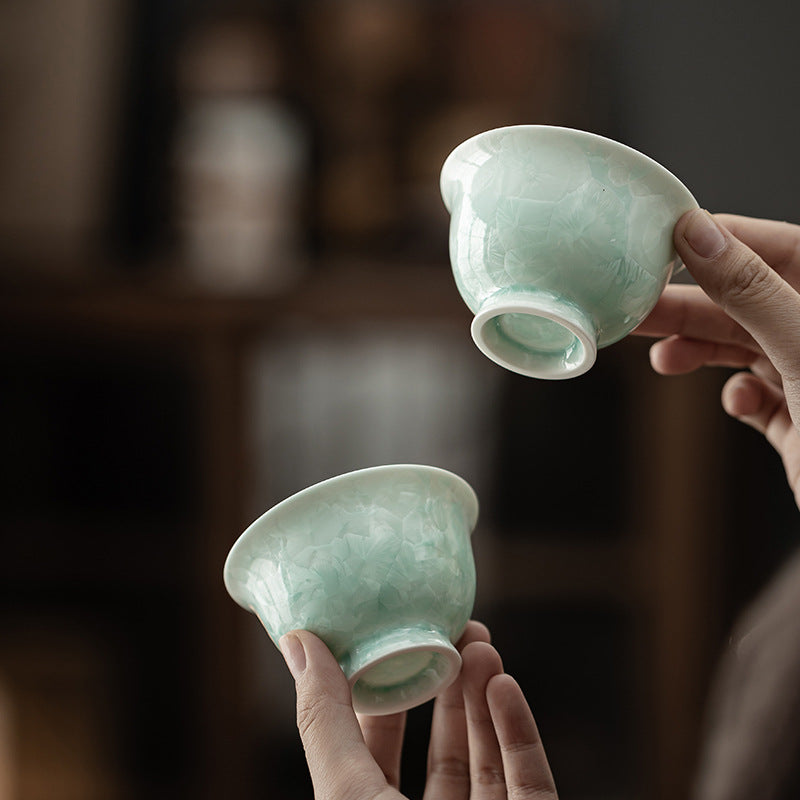Handheld celadon green crystalline glaze ceramic tea cups showing translucent texture