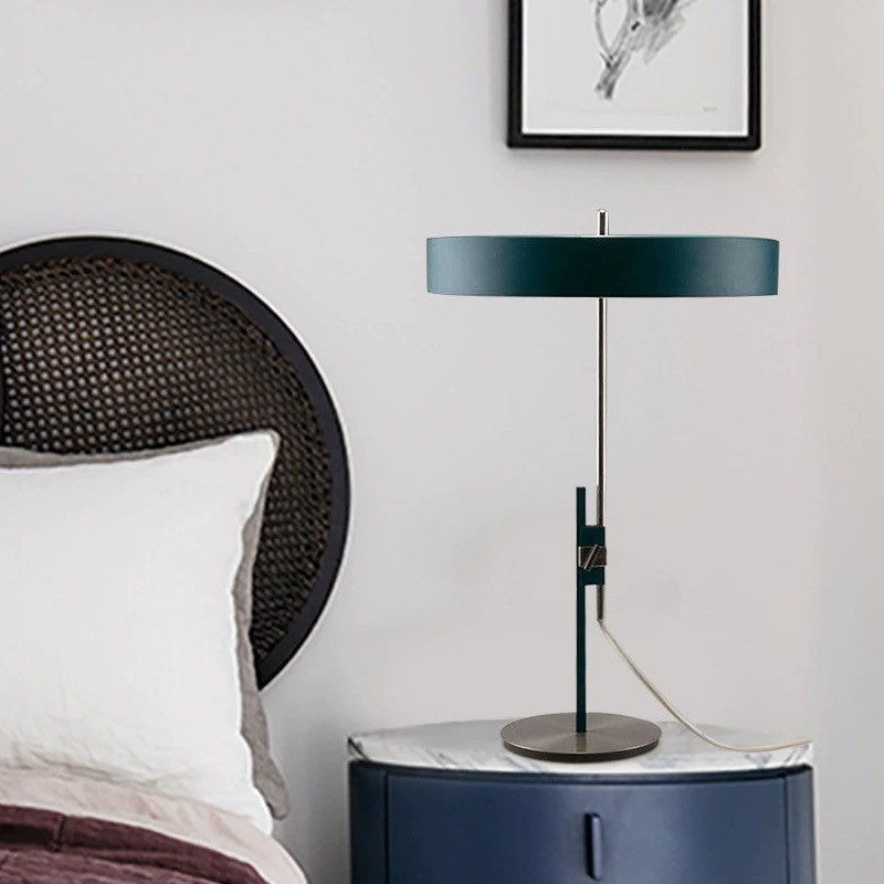 Dark green disc shade designer table lamp styled beside a bed
