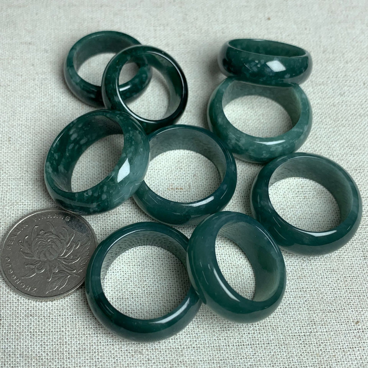 Deep green jadeite wide band rings with coin for scale and natural mottled pattern
