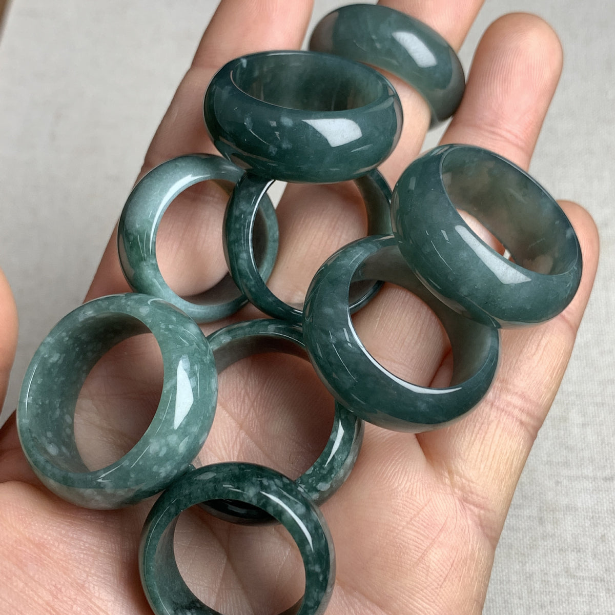 Deep green jadeite wide rings held in hand showing polished luster and stone variation