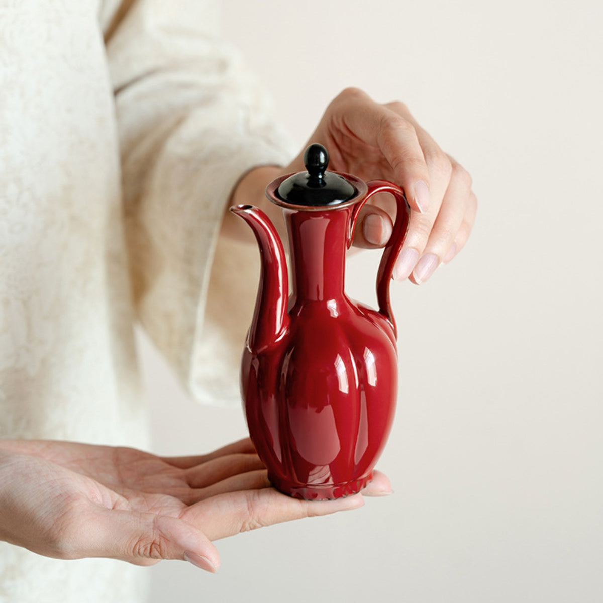 Glossy red Song-inspired ceramic ewer held in the hand
